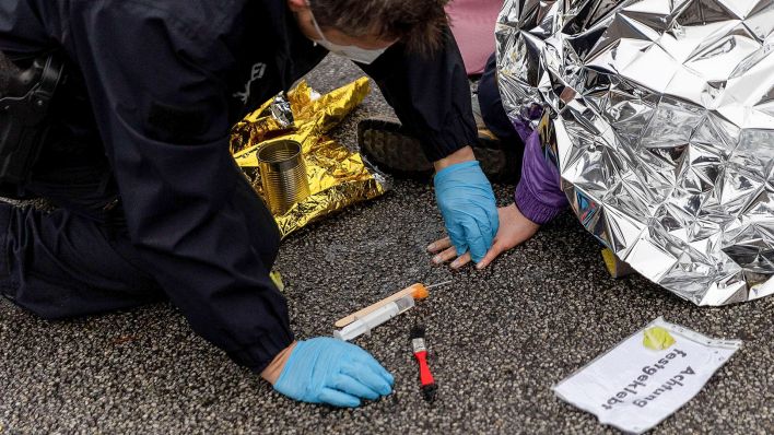 Ein Polizist löst mit einem Lösungsmittel den Klebstoff, mit dem sich ein Aktivist festgeklebt hat, von der Hand und der Fahrbahn (Bild: dpa/Carsten Koall)