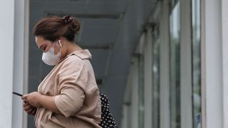 Symbolbild: Eine Frau mit FFP2-Maske blickt auf ihr Handy (Bild: dpa/Donal Husni)