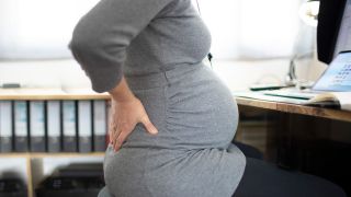 Symbolbild: Junge schwangere Frau am Arbeitsplatz. (Quelle: dpa/U. Grabowsky)