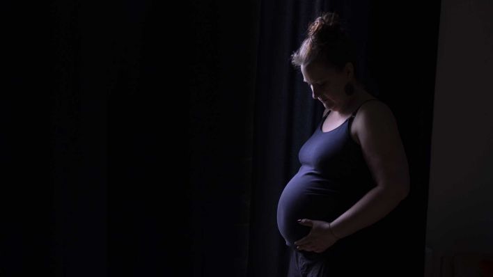 Eine schwangere Frau steht im Dunkeln und hält sich den Bauch (Quelle: dpa/Ute Grabowsky)