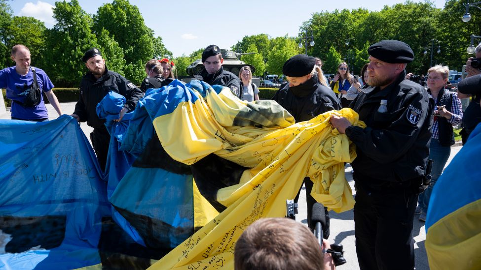 Polizisten wickeln am 08.05.2022 eine groﬂe Ukrainische Fahne bei einer Gedenkveranstaltung vor dem Sowjetischen Ehrenmal im Tiergarten zusammen. (Quelle: dpa/Christophe Gateau)