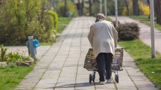 Eine ältere Frau mit Rolator und Einkaufstaschen geht in Berlin einen Gehweg entlang. (Quelle: imago-images/Dirk Sattler)