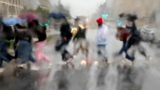 Archivbild: Bei strömenden Regen und Temperaturen um 13 Grad Celsius laufen Menschen am 29.9.2021 mit Regenschirmen über die Straße an der East Side Galerie. (Quelle: dpa/Wolfgang Kumm)
