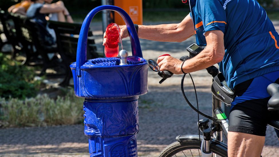 Ein Radfahrer füllt am 18.06.2022 am Tegeler See an einem Trinkbrunnen seine Wasserflasche auf. (Quelle: dpa/Paul Zinken)