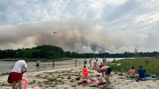 Ausflügler:innen verbringen den heißen Tag am Seddiner See in dem ein Löschhubschrauber wegen des Waldbrandes bei Treuenbrietzen Wasser getankt hat. (Quelle: dpa/S.Pilick)