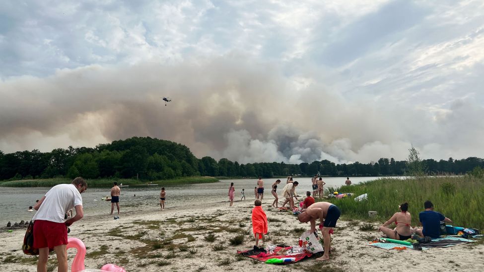 Ausflügler:innen verbringen den heißen Tag am Seddiner See in dem ein Löschhubschrauber wegen des Waldbrandes bei Treuenbrietzen Wasser getankt hat. (Quelle: dpa/S.Pilick)