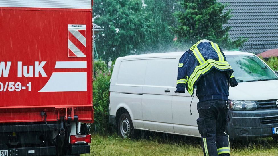 Ein Feuerwehrmann schützt sich mit seiner Einsatzjacke vor dem starken Regen. (Quelle: dpa/A.Riedl)