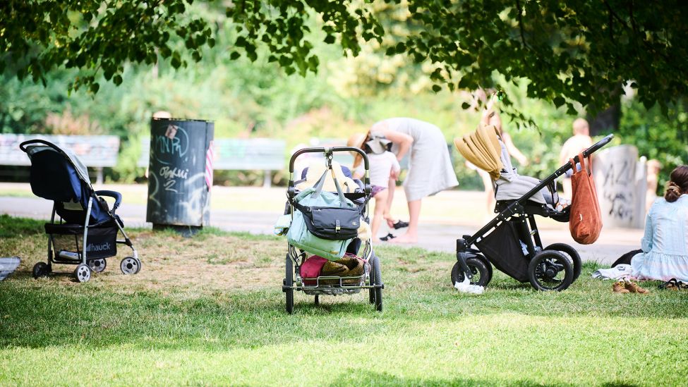 Kinderwägen stehen am 25.06.2022 im Schatten der Bäume, während Eltern mit ihren Kindern an der Wasserstelle im Volkspark am Weinberg spielen. (Quelle: dpa/Annette Riedl)