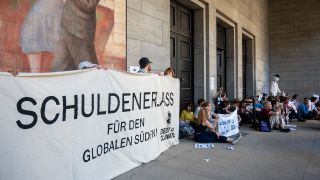 Aktivisten sitzen am 27.06.2022 vor dem Finanzministerium in Berlin und demonstrieren u.a. für einen globalen Schuldenerlass und Klimagerechtigkeit. (Quelle: dpa/Christophe Gateau)