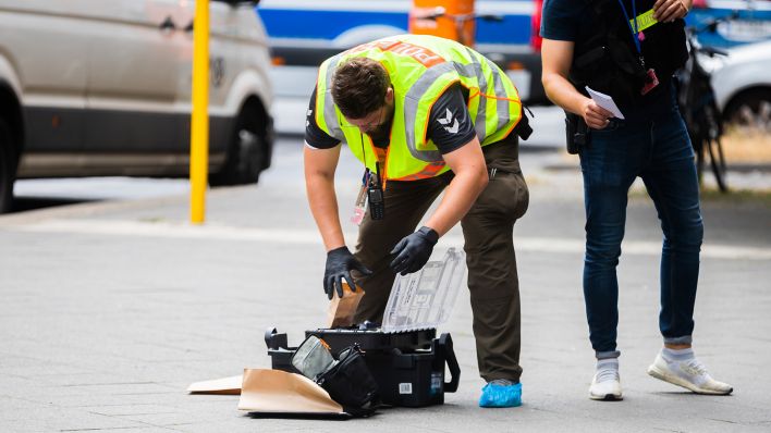 Ein Polizist steht am 29.06.2022 bei einem Polizeieinsatz im Bezirk Wilmersdorf in der Uhlandstraße an einem Koffer der Spurensicherung. (Quelle: dpa/Christoph Soeder)