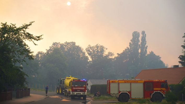 Einsatzfahrzeuge der Feuerwehr werden betankt, während dichter Rauch die Sonne verdeckt. (Quelle: dpa/J.Carstensen)