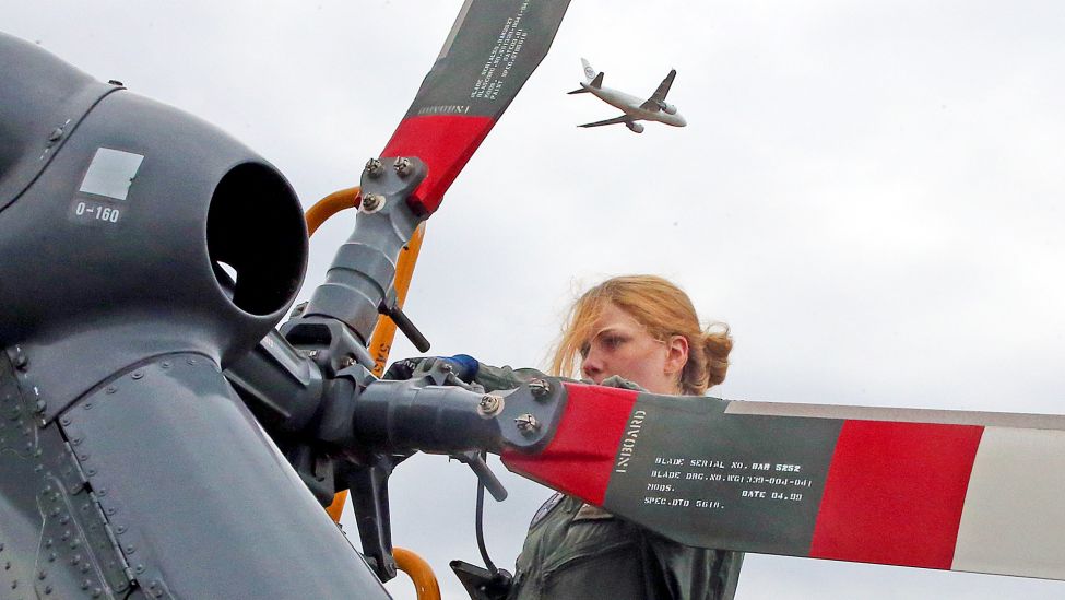 Eine Mechanikerin der Bundesluftwaffe wartet auf der Internationalen Luft- und Raumfahrtausstellung ILA den Heckrotor eines Hubschraubers, während über ihr ein Linienflugzeug startet. (Quelle: dpa/W.Kumm)
