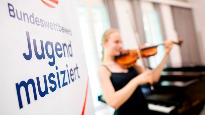 Die Aufschrift „Bundeswettbewerb Jugend musiziert" steht auf einem Plakat, während ein Mädchen ihre Geige spielt. (Quelle: dpa/H.-C.Dittrich)