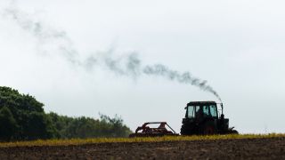 Luftverschmutzung durch die Abgase von einem Traktor, der ueber ein Feld faehrt (Bild: dpa/Florian Gaertner)