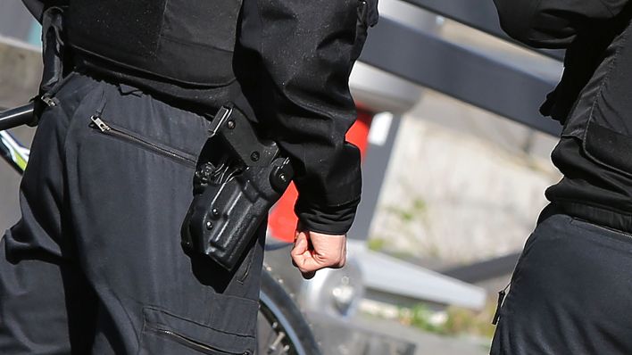 Symbolbild: Polizisten von hinten mit Schusswaffe und kugelsicherer Weste. (Quelle: dpa/Andreas Gora)