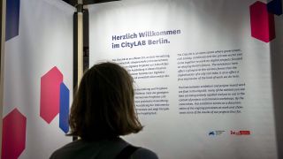 Eine Besucherin steht beim Besuch des CityLAB Berlin vor einer Informationswand. (Quelle: dpa/Paul Zinken)