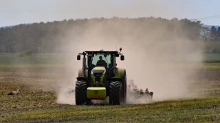 Ein Landwirt bearbeitet den trockenen Boden auf einem Feld und wirbelt dabei viel Staub auf. (Quelle: dpa/Patrick Pleul)