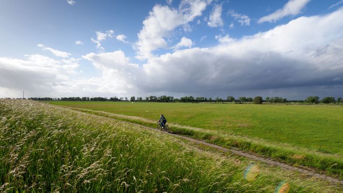Eine Frau fährt Fahrrad in Brandenburg. Im Hintergrund sind dunkle Wolken zu sehen. (Quelle: dpa/Soeren Stache)