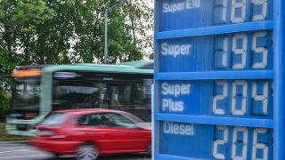 Ein Auto und ein Bus fahren am frühen Morgen an einer Anzeigetafel für Preise von Kraftstoffen einer Tankstelle vorbei. (Quelle: dpa/Patrick Pleul)