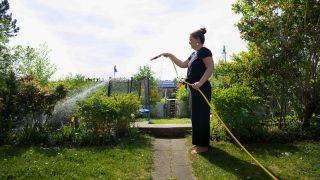 Symbolbild: Frau wässert ihren Garten mit einem Gartenschlauch. (Quelle: dpa/U. Gabowsky)