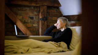 Eine Frau liegt auf der Couch und schaut ein Video auf ihrem Laptop an (Bild: imago images/Thomas Trutschel)