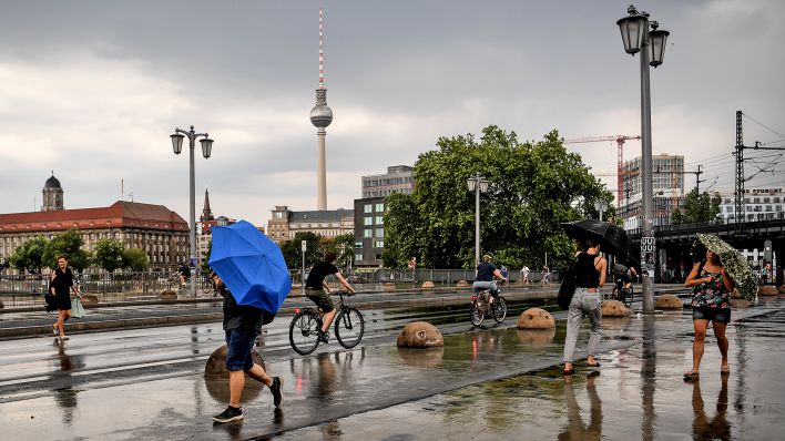 Archivbild: Passanten versuchen sich im Juli 2019 in Berlin mit Regenschirmen zu schützen. (Quelle: dpa/Britta Pedersen)