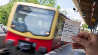 Symbolbild: Ein 9-Euro-Ticket ist vor dem Hintergrund einer einfahrenden S-Bahn zu sehen. (Quelle: dpa/M. Skolimowska)