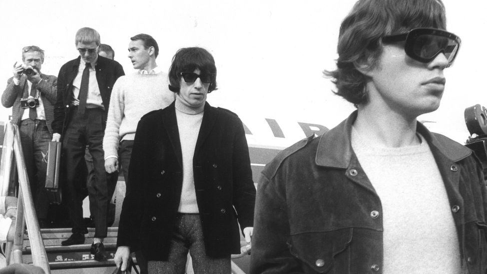 Frontmann Mick Jagger (r) und Bassist Bill Wyman (dahinter) verlassen am Nachmittag des 15.09.1965 auf dem Flughafen Tegel das Flugzeug, das sie aus München nach Berlin gebracht hat. (Quelle: dpa/Konrad Giehr)