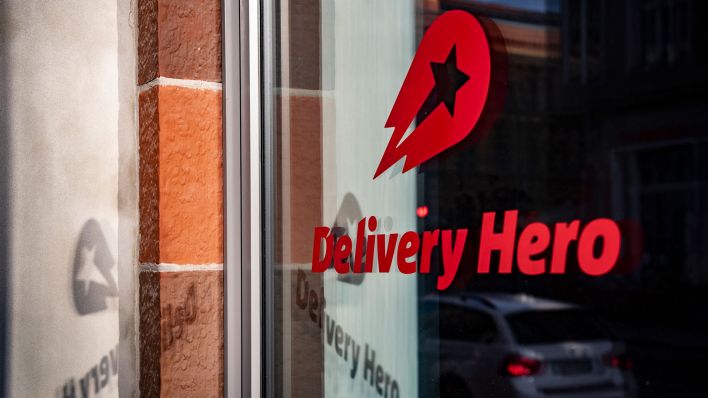 Das Logo und der Schriftzug des Essenslieferdienstes Delivery Hero spiegelt sich in einer Fensterscheibe am Firmensitz. (Quelle: dpa/Paul Zinken)
