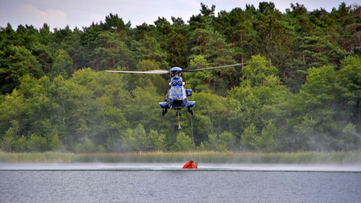 Ein Hubschrauber tankt Löschwasser zur Bekaämpfung des Waldbrands im ehemaligen Truppenübungsplatz. (Quelle: dpa/Christian Guttmann)