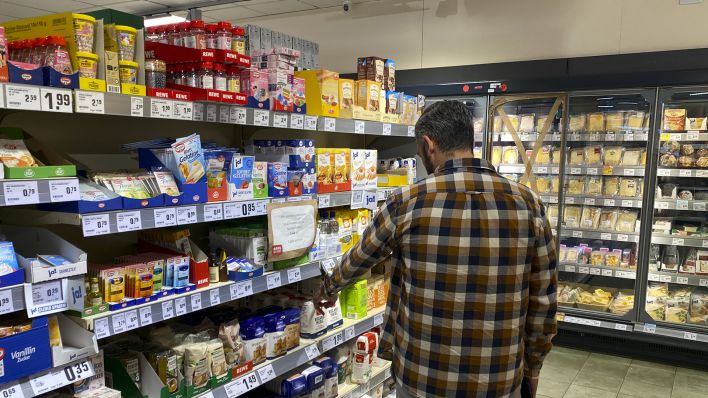 Symbolbild: Ein Mann steht in einem Supermarkt und vergleicht die Preise. (Quelle: dpa/Hosbas)