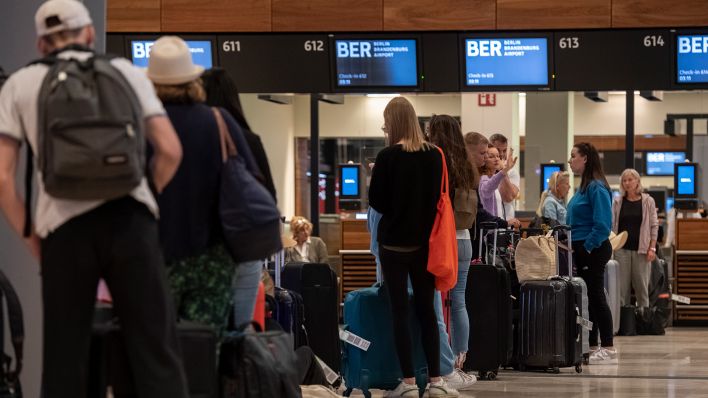 Reisende stehen am 27.07.2022 am Flughafen BER am frühen Morgen an einem Check-In-Schalter (Quelle: dpa/Paul Zinken)