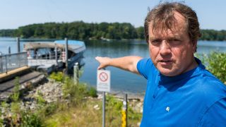Der Strausberger Anwalt Jens Mader zeigt auf das Wasser des Straussees und schaut dabei in die Kamera, 20.07.2022 (Quelle: rbb / Hinze).