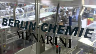 Der Schriftzug "Berlin-Chemie Menarini" steht auf einer Glasscheibe, durch die man in die Produktionshalle des Berliner Pharmaunternehmen sehen kann. (Quelle: rbb)