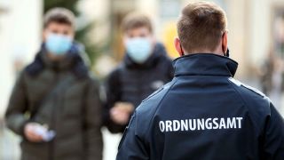 Archiv: Ein Mitarbeiter vom Ordnungsamt patrouilliert in der Fußgängerzone an Passanten vorbei, die Mund-Nase-Bedeckung tragen. (Foto: Friso Gentsch/dpa)