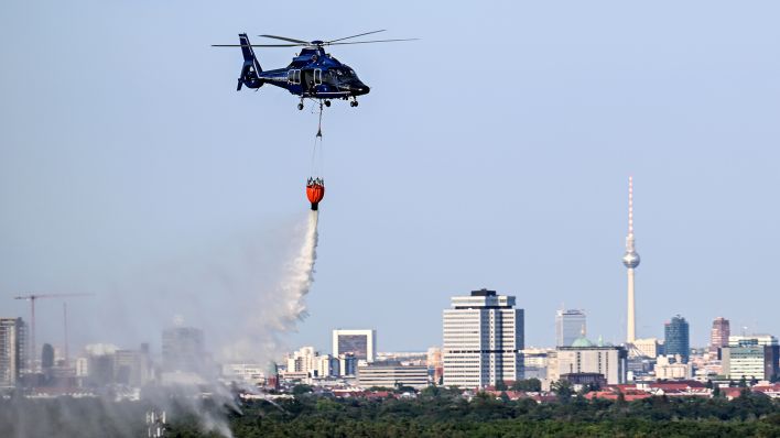 Ein Hubschrauber der Bundespolizei wirft am 09.08.22 Wasser über der Brandstelle im Grunewald ab (Quelle: dpa/Britta Pedersen)