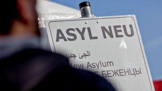 Symbolbild:Ein Geflüchteter steht vor einem Schild mit der Aufschrift "Asyl Neu".(Quelle:dpa/M.Kappeler)