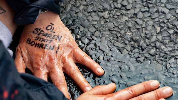 "Öl sparen statt bohren" steht auf der Hand einer Demonstrantin der Gruppe "Letzte Generation", die sich auf dem Asphalt felstgeklebt hat.(Quelle:dpa/P.Zinken)