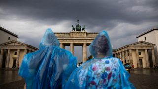 Zwei Personen stehen mit Plastikregenschutz vor dem Brandenburger Tor. (Quelle: dpa/Christoph Soeder)
