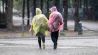 Passanten mit Plastik-Regenschutz gehen nahe des Brandenburger Tors durch den Regen. (Quelle: dpa/Christoph Soeder)