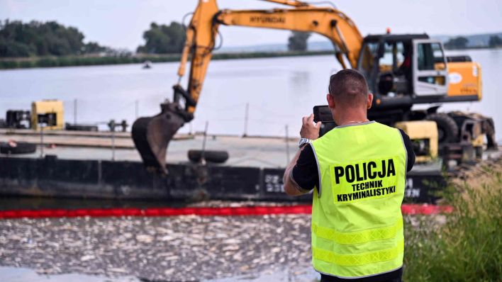 Ein Polizist macht ein Foto eines Baggers der tote fische aus der Oder schaufelt. (Foto: Marcin Bielecki/PAP)