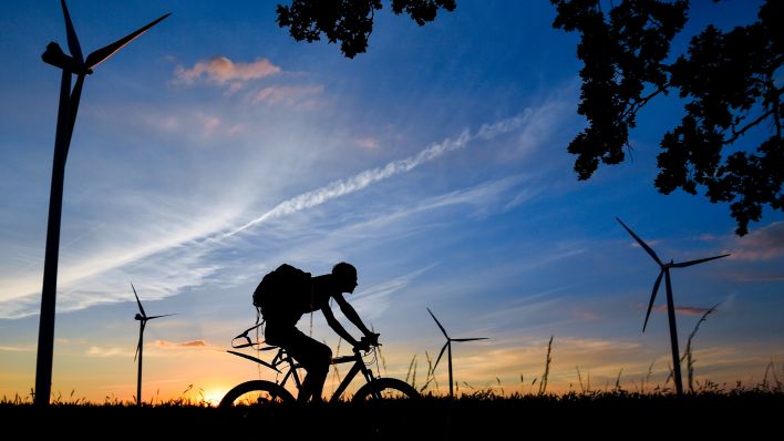 Archiv: Ein Radfahrer ist bei Sonnenuntergang vor Windenergieanlagen am 29.06.2016 auf einem Radweg nahe Sieversdorf im Landkreis Oder-Spree (Brandenburg) unterwegs. (Foto: Patrick Pleul /dpa)