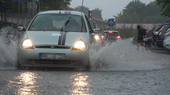 Ein Auto fährt in Nauen über eine Straße auf der sich Regenwasser gestaut hat