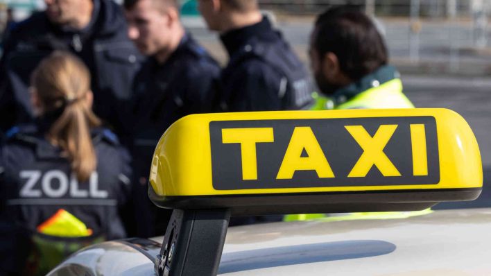 Taxi-Schild mit Zollbeamten im Hintergrund. (Foto: Hannes P. Albert/dpa )