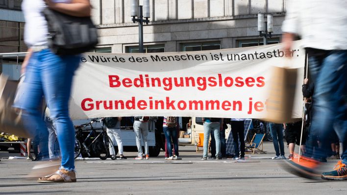 Archivbild: «Bedingungsloses Grundeinkommen jetzt!» steht bei der Auftaktkundgebung einer Demonstration für ein bedingungsloses Grundeinkommen auf dem Alexanderplatz auf einem Banner geschrieben. (Quelle: dpa/C. Soeder)