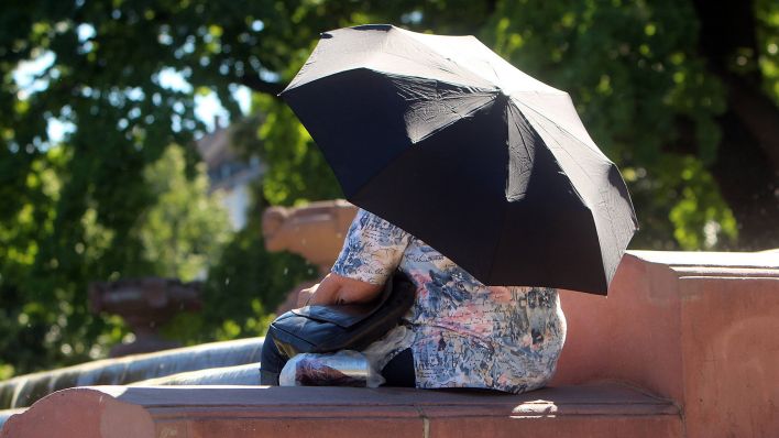 Sommerhitze: Frau schützt sich vor der Sonne mit einem Regenschirm und nimmt ein Fußbad im Wasser des Brunnens. (Quelle: imago images)