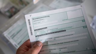 Eine Person hält das Formular für die Grundsteuer in der Hand (Bild: dpa/K. Schmitt)