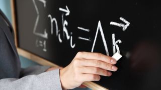 Symbolbild: Eine Lehrerin schreibt an der Tafel im Klassenzimmer (Quelle: IMAGO/YAY Images)