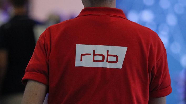 Symbolbild: Ein Mann trägt ein T-Shirt mit dem rbb-Logo (Quelle: IMAGO/Matthias Baran)