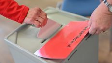 Symbolbild/bearbeitet: Eine Frau wirft ihren Stimmzettel in die Wahlurne (Quelle: dpa/Felix Kästle)